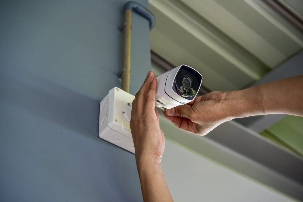 Hands installing a white security camera on a wall, preparing for professional CCTV monitoring services.